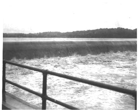 Water flowing over a dam; handrail in lower left corner